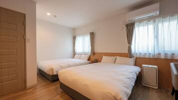 A hotel room with two beds, a wooden wardrobe, an air conditioning unit, and a window with curtains.