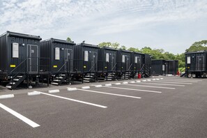 A row of black portable cabins with white numbers on doors, arranged in a parking lot with white lines on the ground. - HOTEL R9 The Yard Sosa (Sosa)