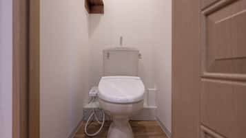 A small, clean bathroom with a white toilet, a wooden floor, and a wall-mounted shelf.