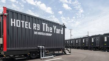A large black container with "HOTEL R9 The Yard" and "RS HOTELS GROUP" written on it, parked in a lot with other similar containers.