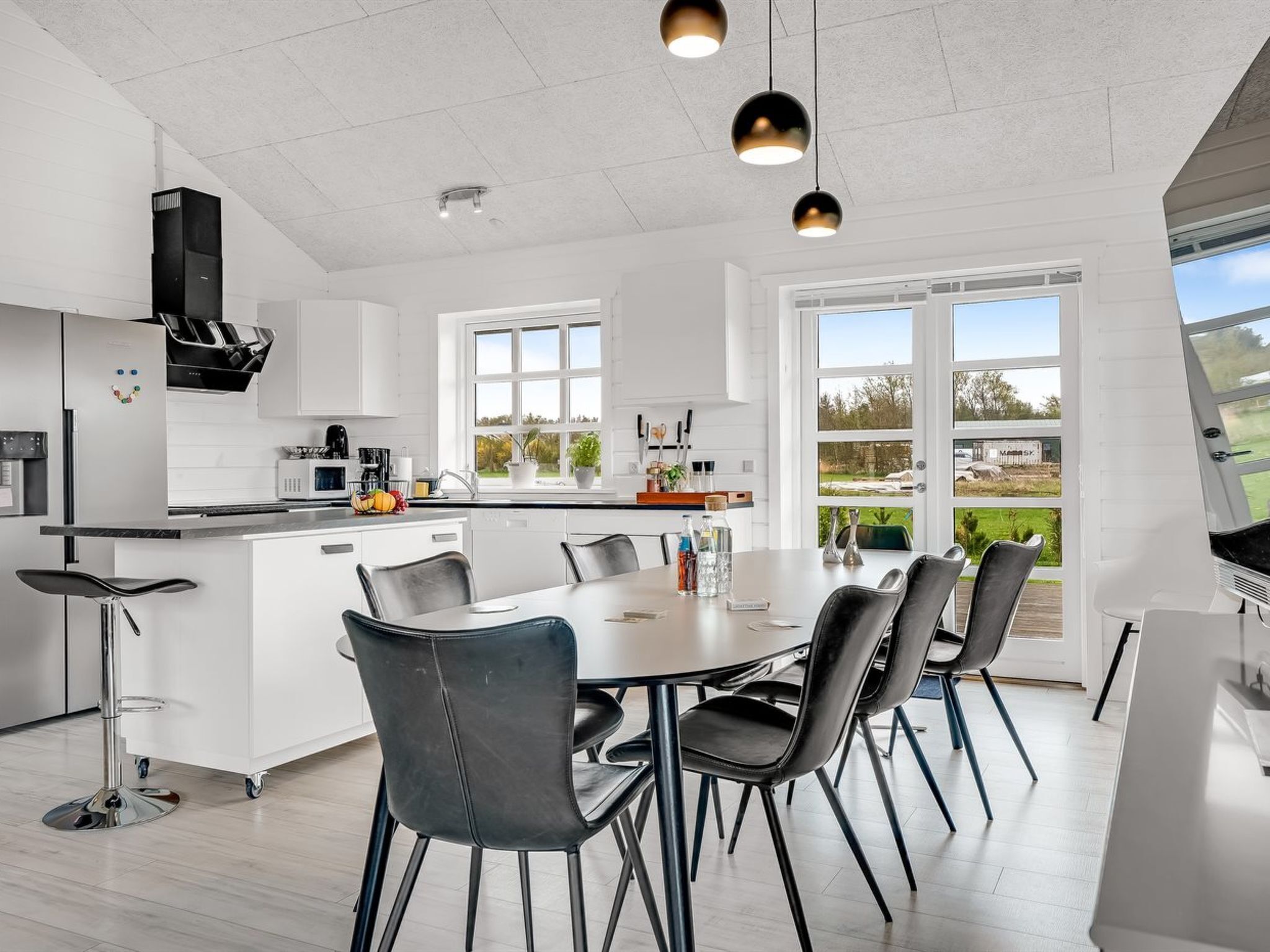 Una cocina moderna con armarios blancos, una isla central y un área de comedor con sillas negras.