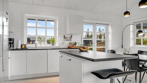 Uma cozinha moderna com armários brancos, uma ilha central e um espaço de jantar com cadeiras pretas.