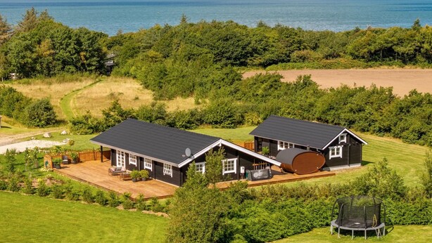 Uma casa de dois andares com uma varanda grande e um trampolim, rodeada por vegetação exuberante e vista para o mar.