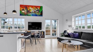 Uma sala de estar ampla, com uma televisão grande, uma mesa de jantar e um sofá.