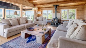 Ein gemütliches Blockhaus-Interieur mit einer großen Holzbalkendecke, zwei Sofas, einem Couchtisch und einem Kaminofen.