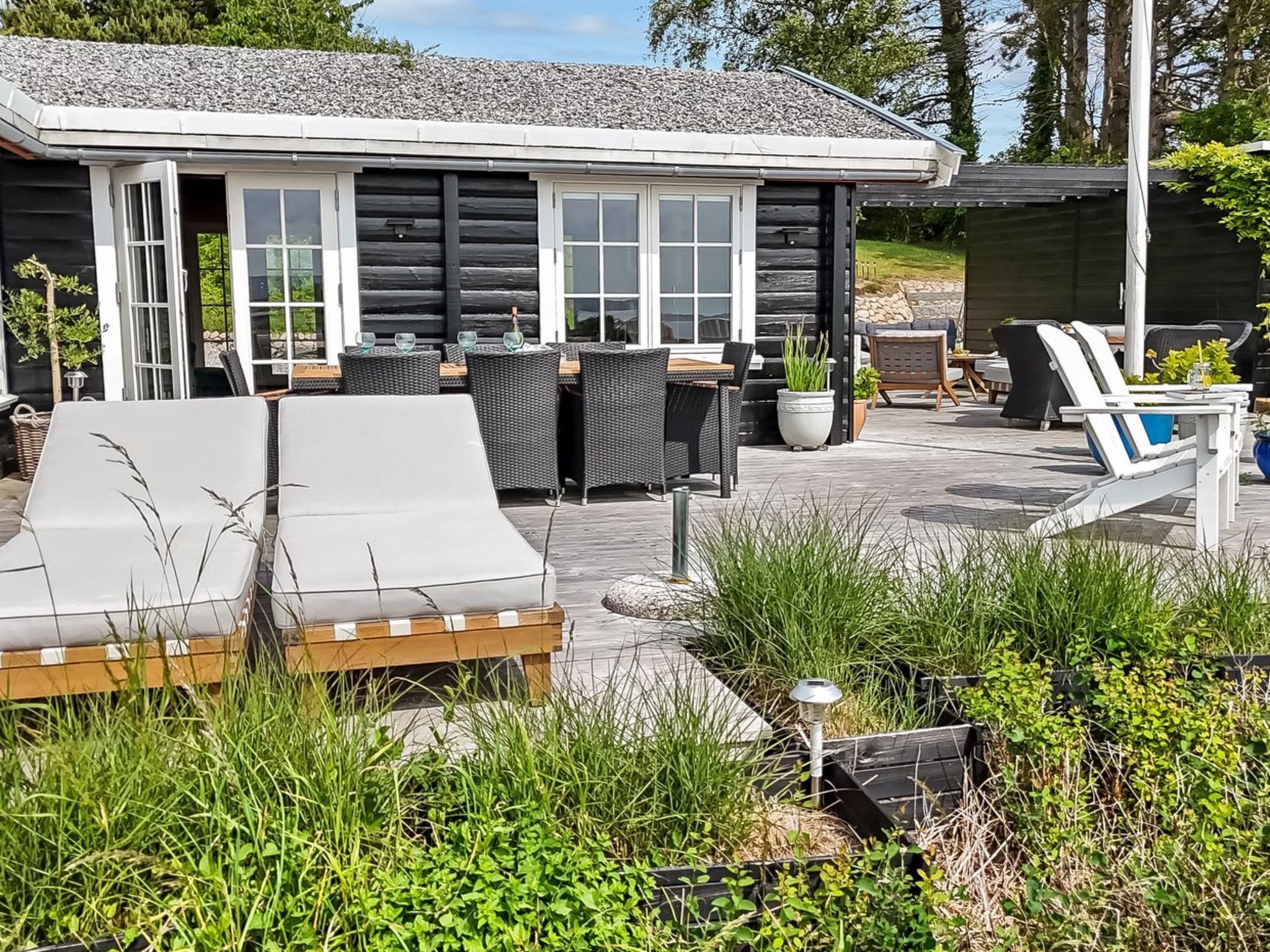 Uma cabana de madeira com um terraço, mobiliário externo e um pequeno jardim.
