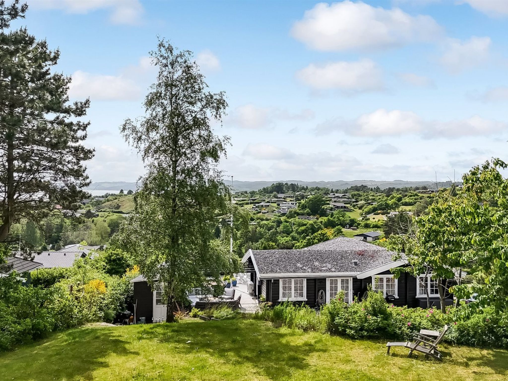 A house with a sloped roof, surrounded by a well-maintained lawn and dense greenery.