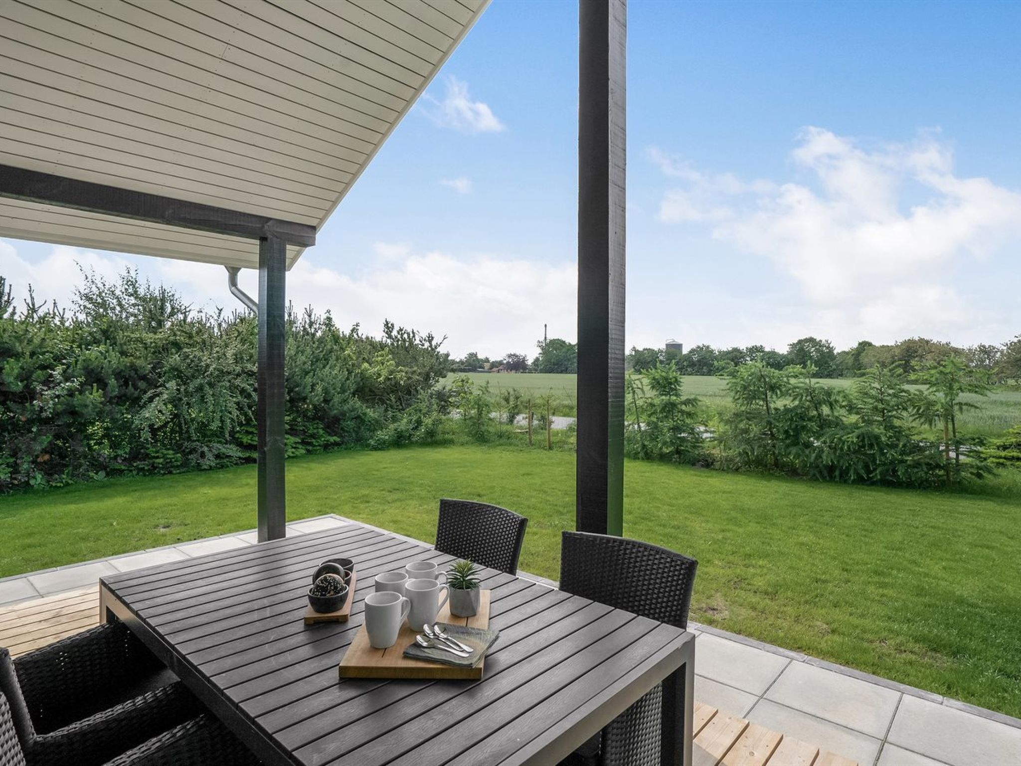 An outdoor patio with a table set for dining, surrounded by greenery and a clear view of the countryside.
