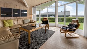 Una habitación amplia con techo alto, un ventanal, un sofá, una mesa de centro y un sillón mecedora.
