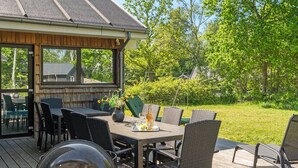 An outdoor patio with a wooden deck, a covered seating area, and a grill.
