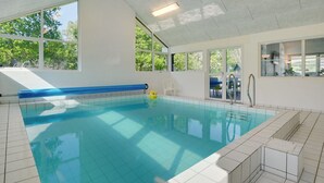 An indoor swimming pool with clear blue water, surrounded by white tiled walls and a high ceiling.