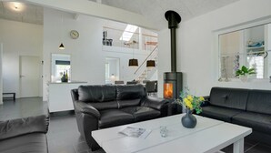 A modern living room with a fireplace, leather sofas, a white coffee table, and a kitchen area in the background.