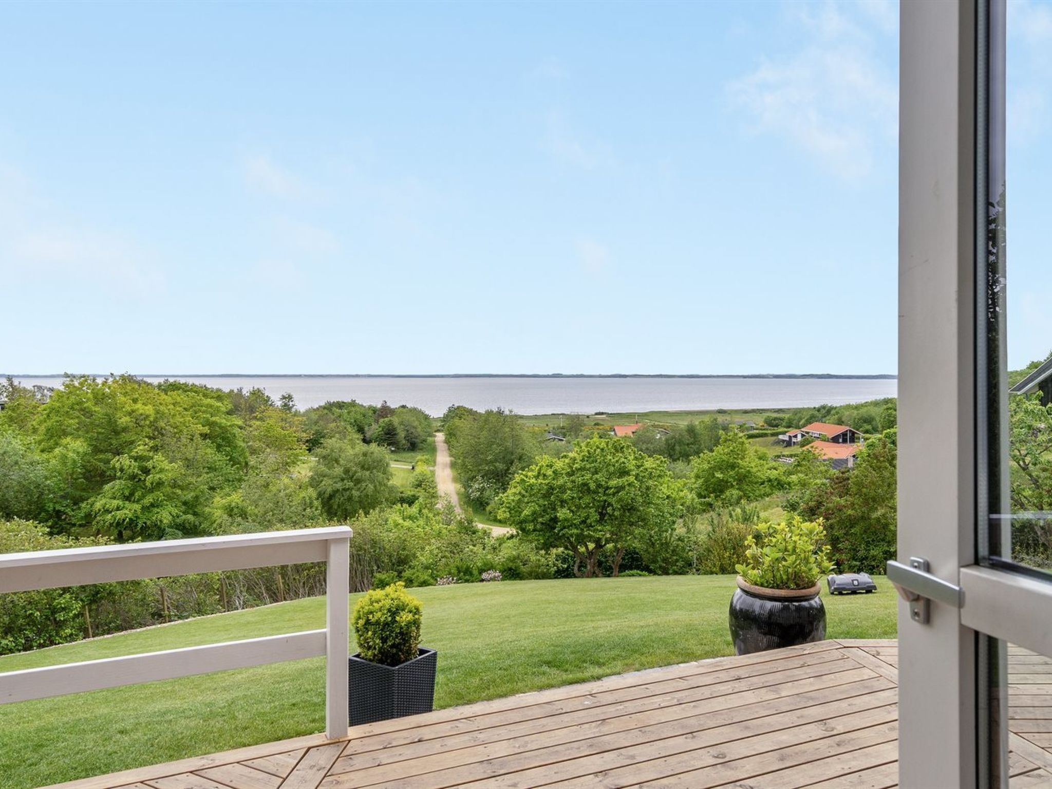 Ein Balkon mit Blick auf ein Gewässer, viel Grün und eine entfernte Küste.