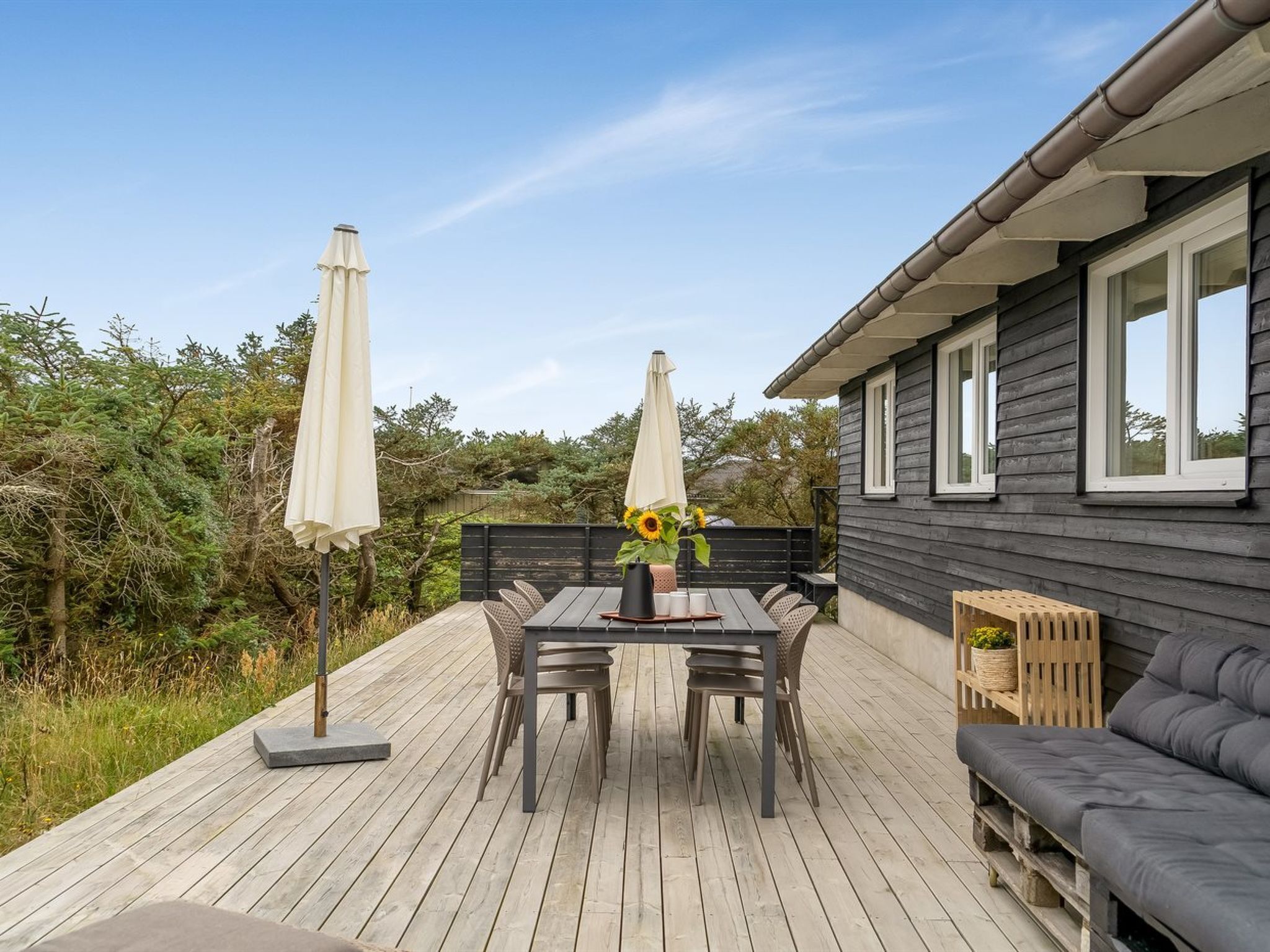 A deck with a table and chairs, a sofa, and two umbrellas.