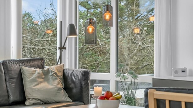 Una sala de estar moderna con un sofá de cuero, una mesa de centro de madera con un cuenco de fruta y un ventanal con vistas a árboles.