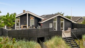 Una casa moderna de dos pisos con fachada oscura, un espacio de estar techado al aire libre y una escalera que lleva a una terraza.
