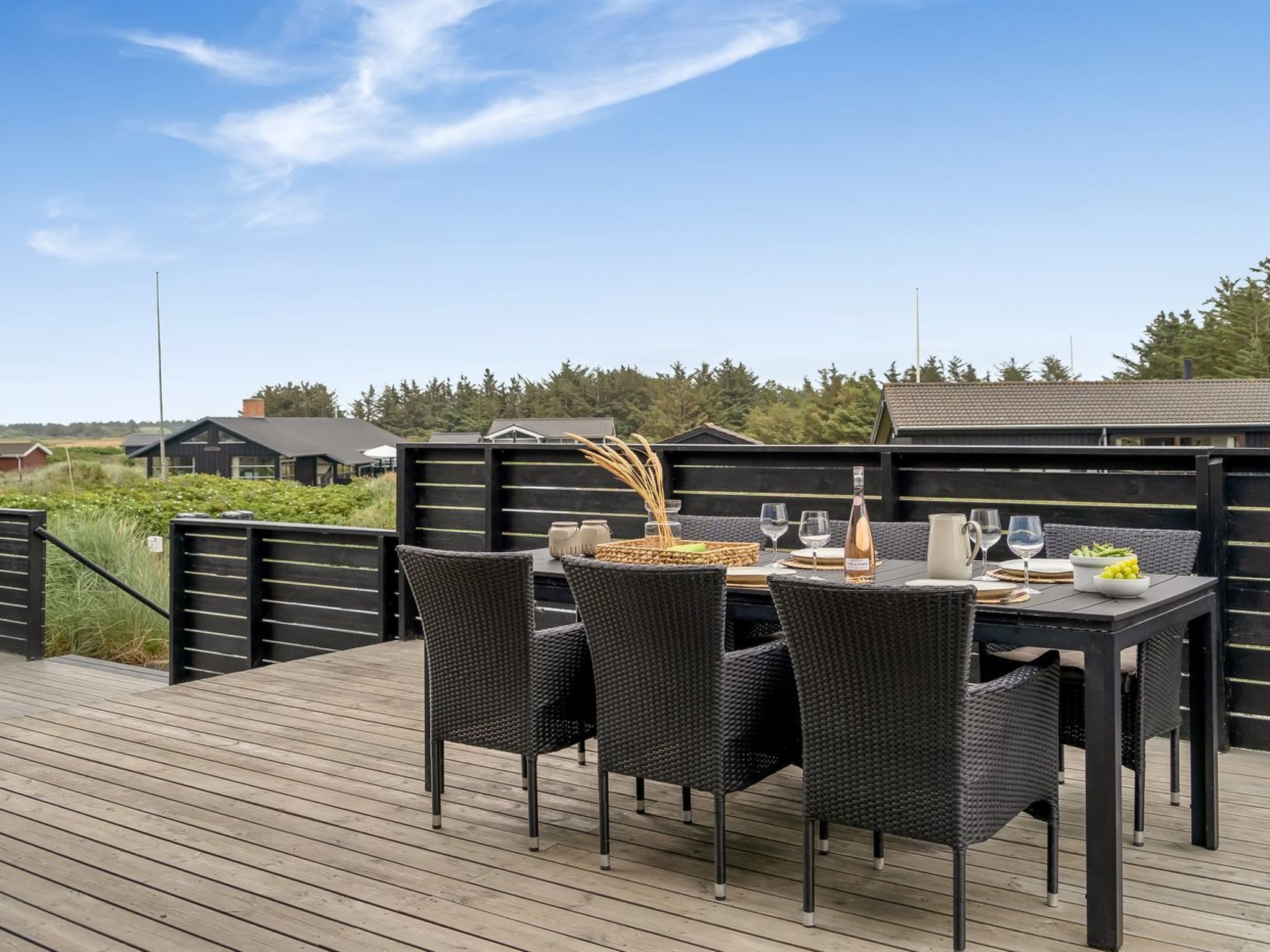 Una terraza de madera con una mesa lista para comer, rodeada de sillas de mimbre.