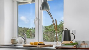 Una cocina moderna con ventana, un lavamanos, una tetera y una tabla de cortar con verduras.