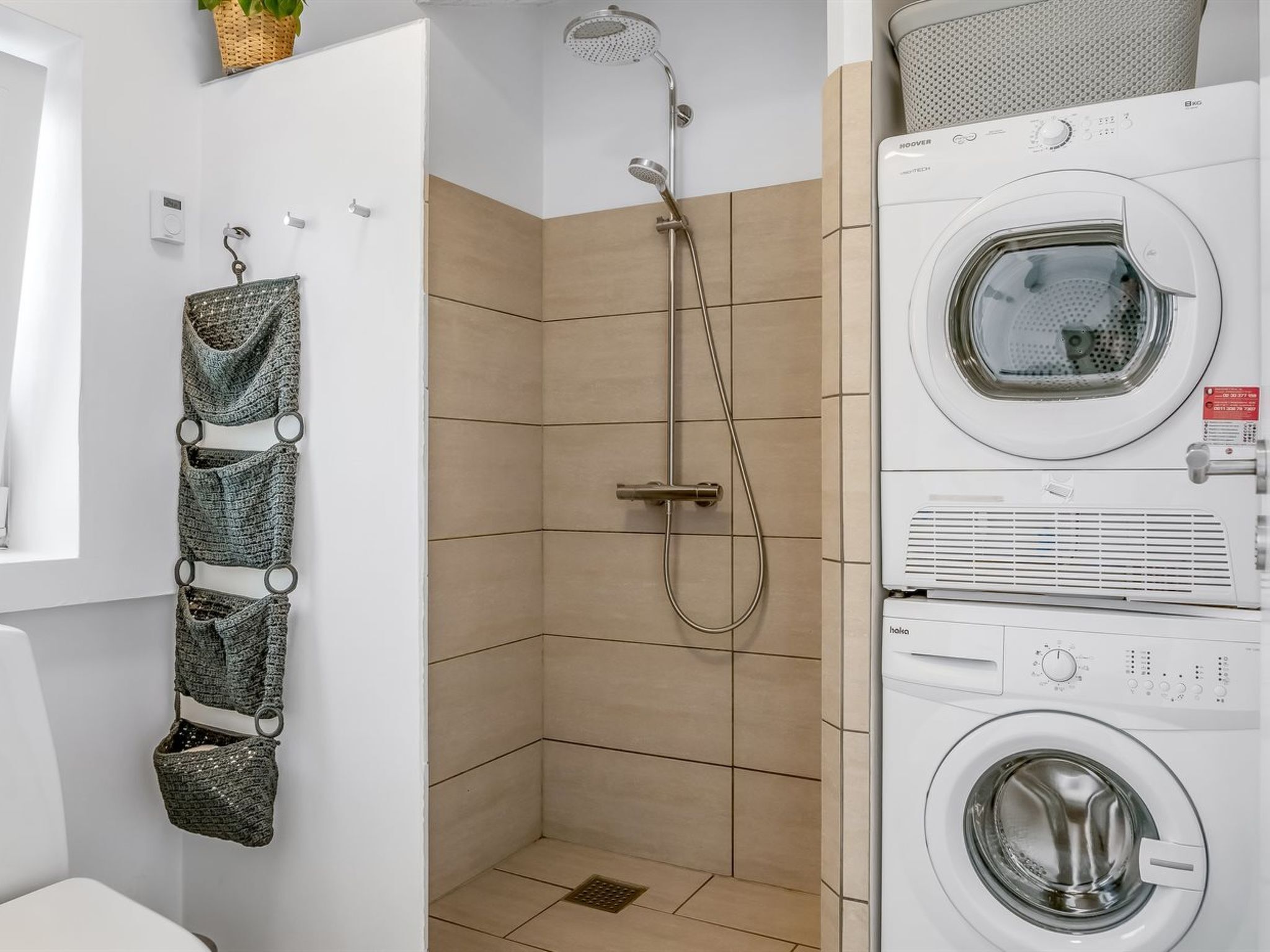Un baño pequeño con ducha, lavadora integrada y un tendedero.
