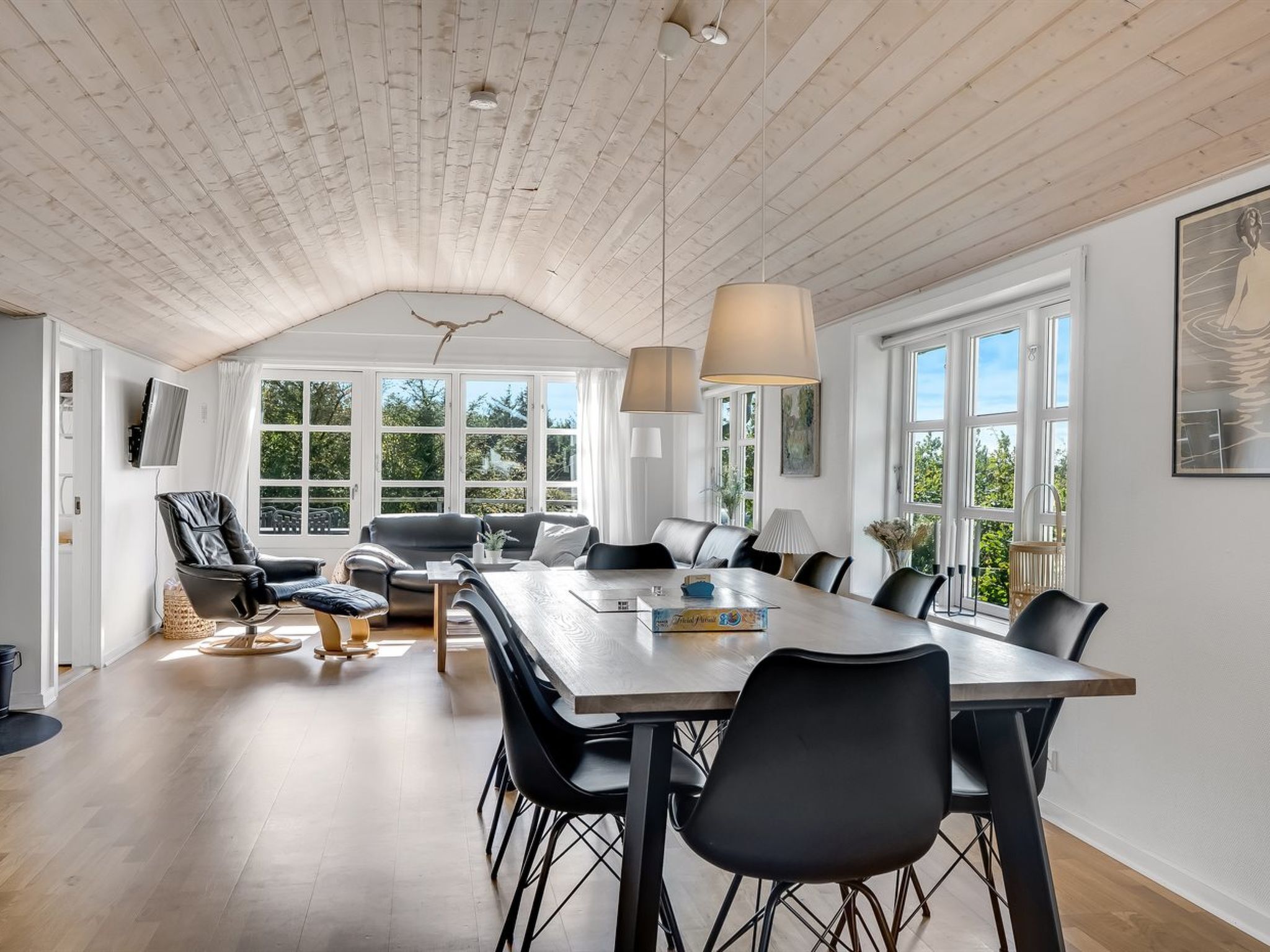 A spacious dining area with a long table and multiple chairs, a sofa, and a television mounted on the wall.