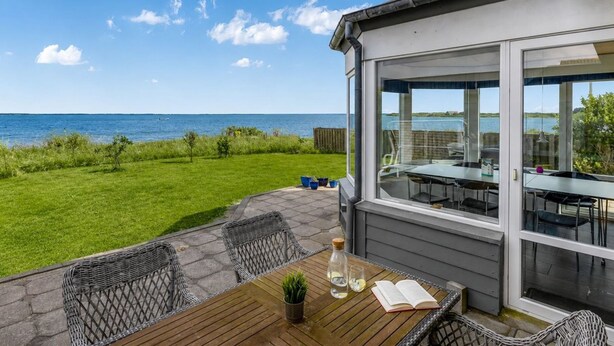 A patio with a table and chairs, a view of the sea, and a building with large windows. - "Bibbi" - 20m to the fjord by Interhome (Ulfborg)