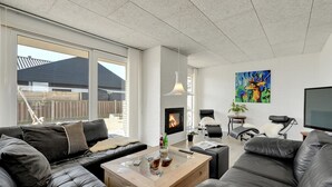 A modern living room with leather sofas, a fireplace, a television, and a large window offering a view of the outside. - "Bibbi" - 20m to the fjord by Interhome (Ulfborg)