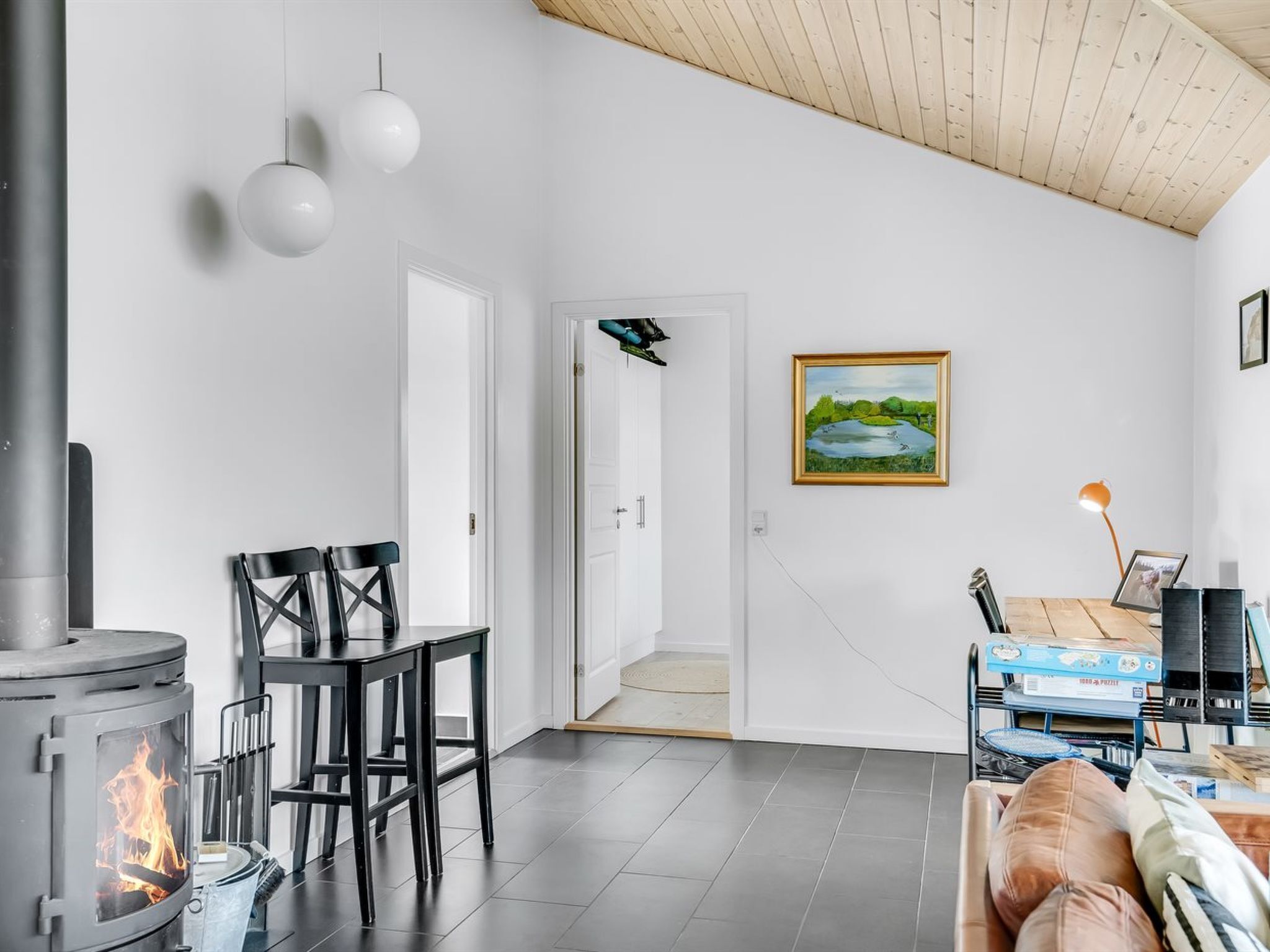 Un salon moderne avec un poêle à bois, une table à manger avec des chaises, un canapé et un tableau accroché au mur.