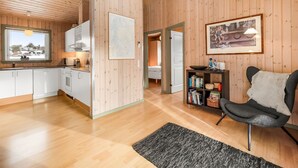A modern interior with wooden walls, a kitchen with white cabinets, a dining area with a black chair, and a bookshelf.