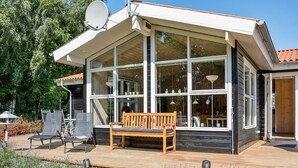 A modern house with a large glass extension, a wooden deck with outdoor furniture, and a satellite dish.