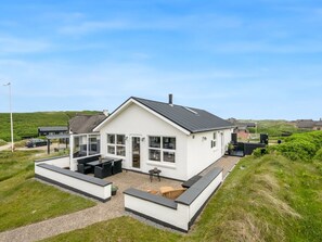 Een wit huis met een zwart dak, een terras met zitplaatsen en een oprit met grind.
