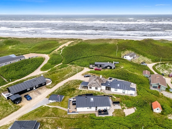 An aerial view of a coastal residential area with houses, a road, and the ocean in the background.