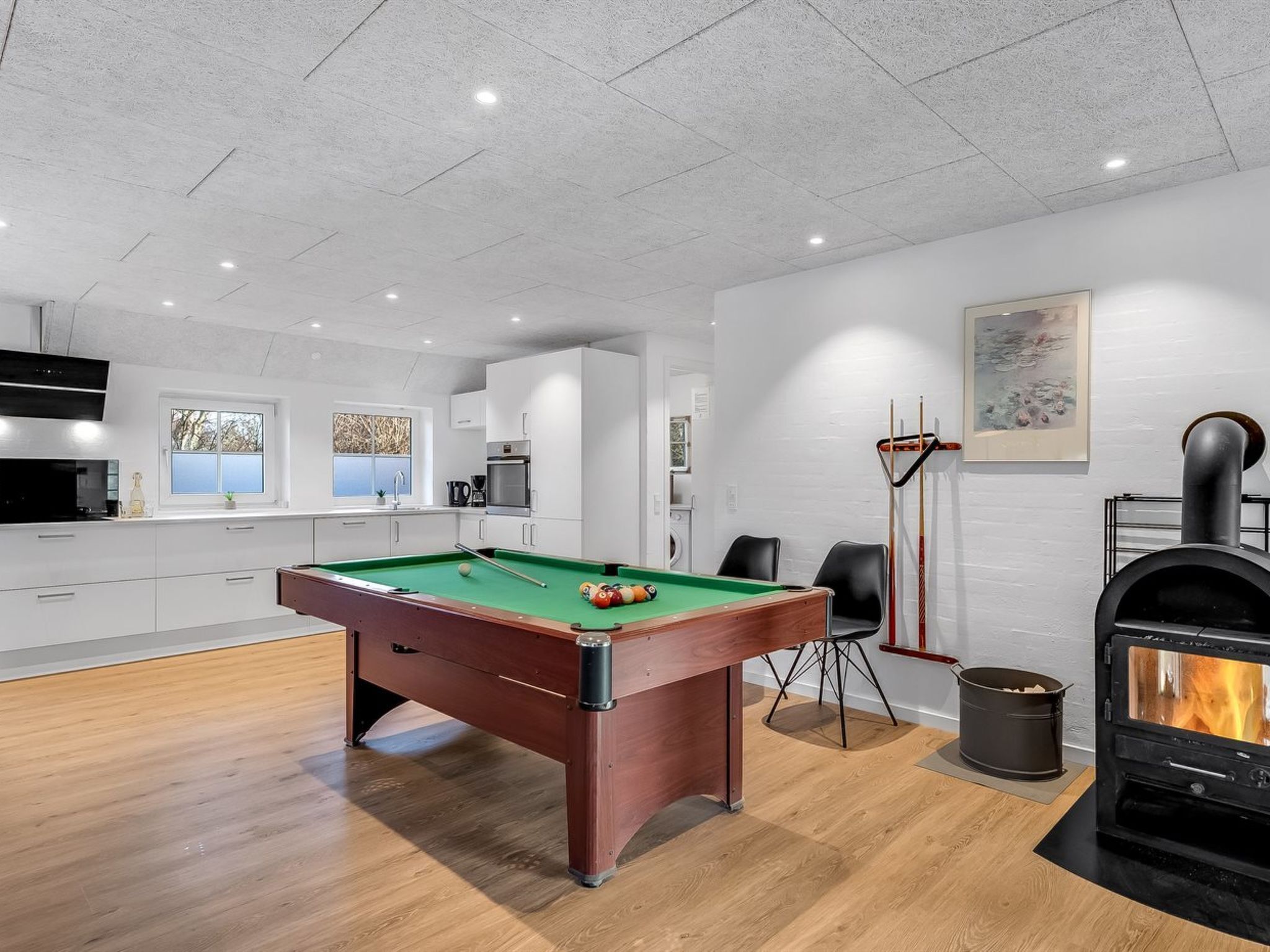 A modern kitchen with a pool table, a fireplace, and a dining area with chairs.
