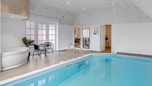 A spacious indoor swimming pool with a clear view of the adjacent room, a wooden ceiling, and a seating area with chairs and a table. - "Thana" - 1.4km from the sea by Interhome (Ulfborg)
