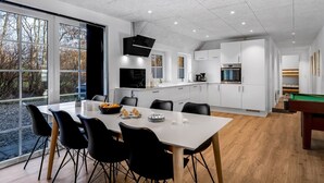 A modern kitchen with white cabinets, a dining area with a white table and black chairs, and a pool table in the corner. - "Thana" - 1.4km from the sea by Interhome (Ulfborg)