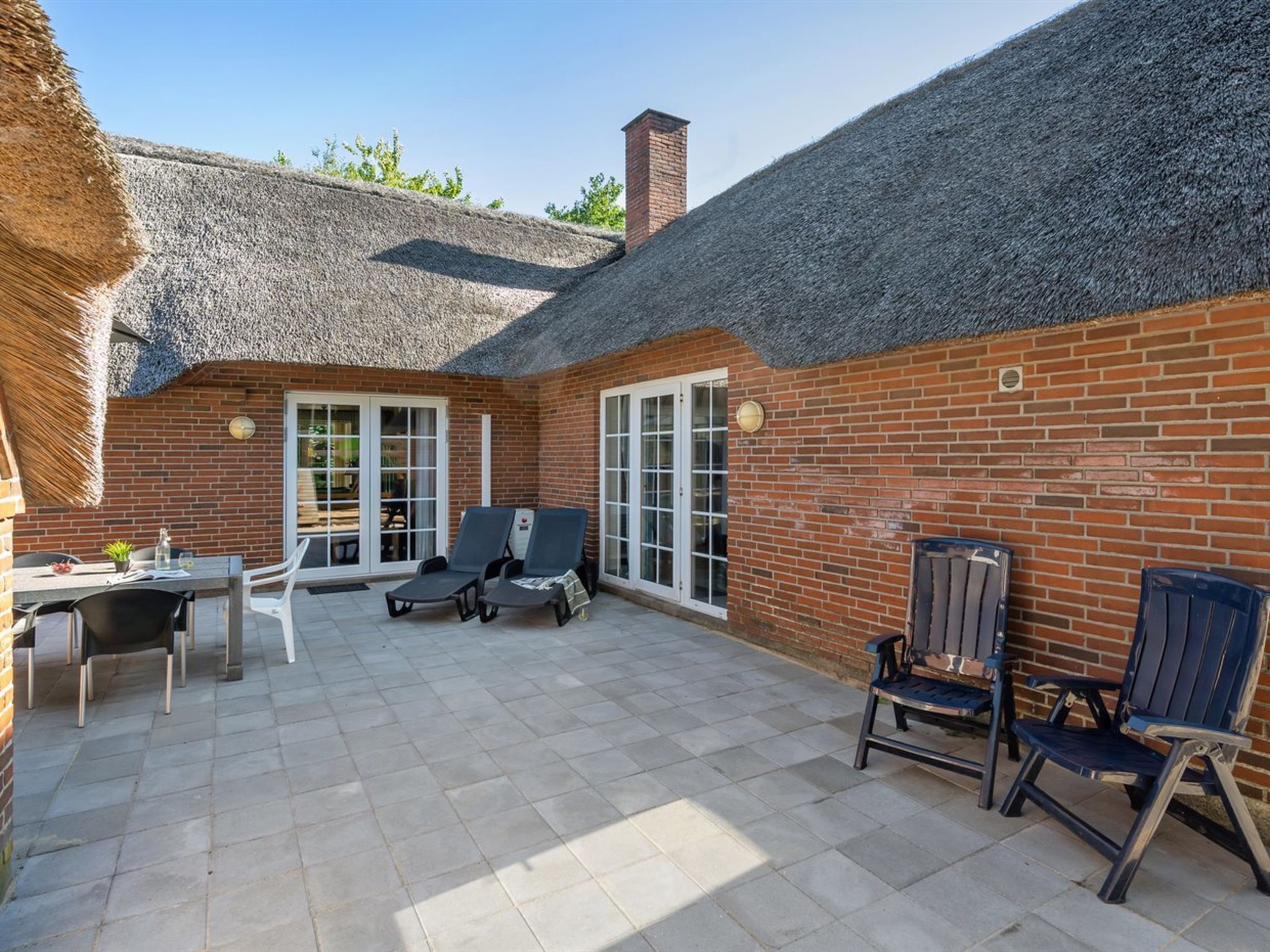 Eine Terrasse mit Ziegelmauer, einem Reetdach und einem Tisch mit Stühlen.
