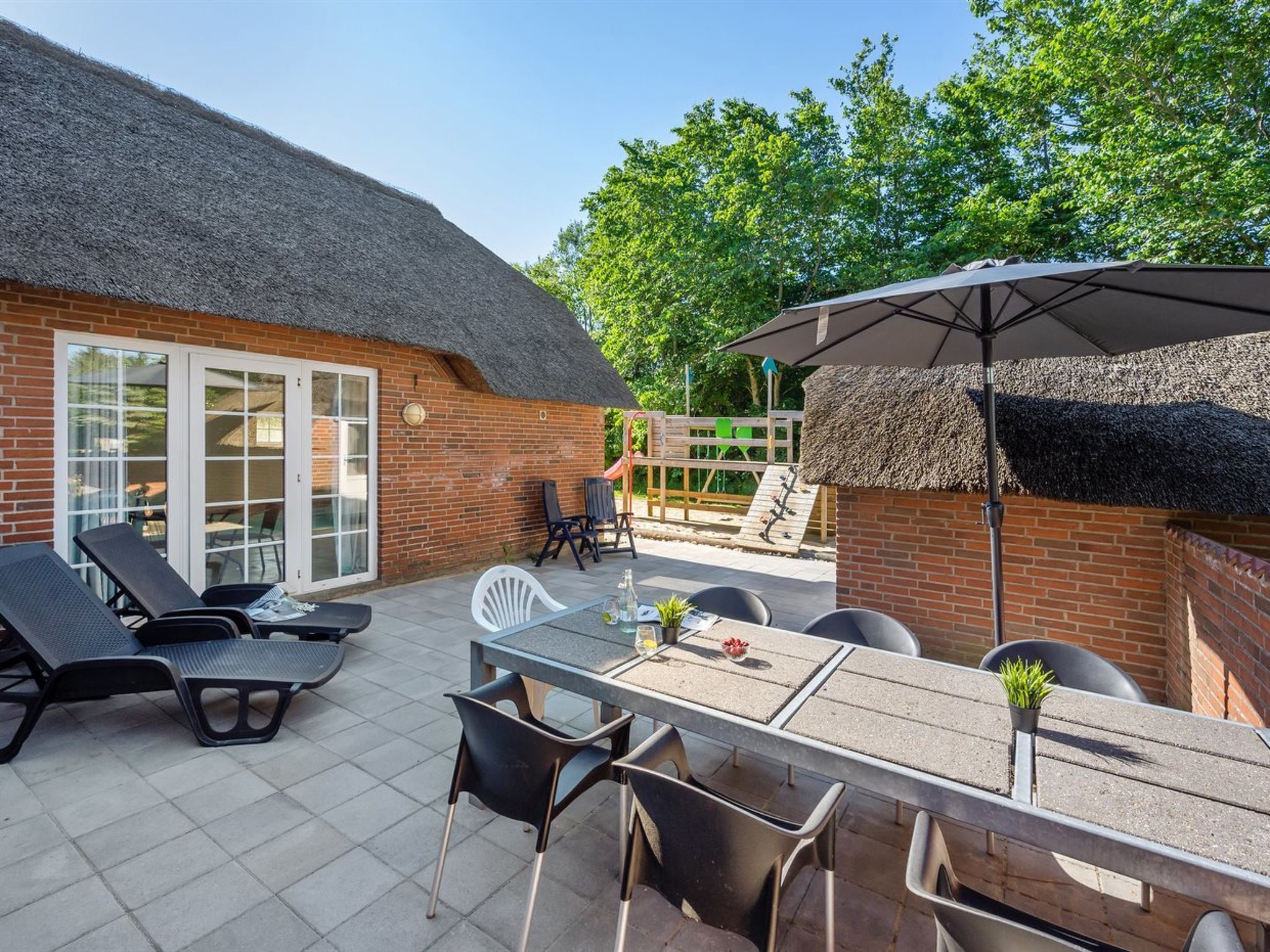 Een terras met een tafel en stoelen, een rieten dakconstructie en een bakstenen muur.