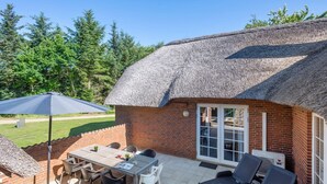 A patio with a table and chairs, a thatched roof structure, and a brick wall. - "Thana" - 1.4km from the sea by Interhome (Ulfborg)