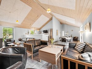 Een ruime woonkamer met een hoge nok, houten balken en een eethoek met moderne meubels.