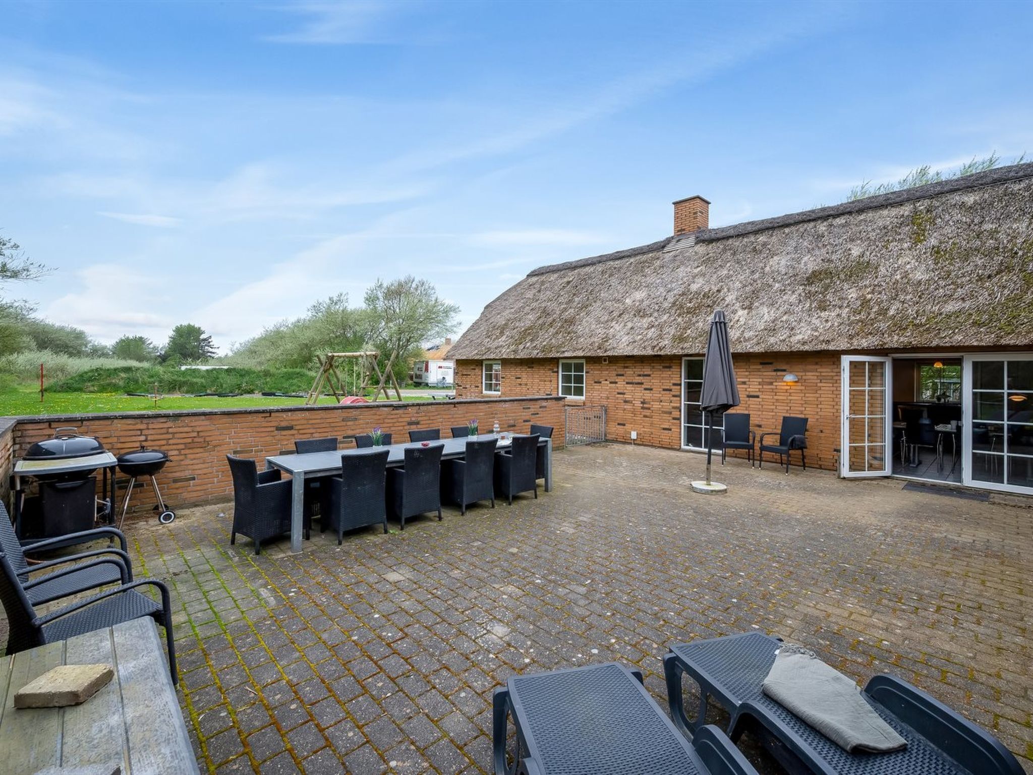An outdoor patio area with brick flooring, a thatched-roof building, and outdoor seating.