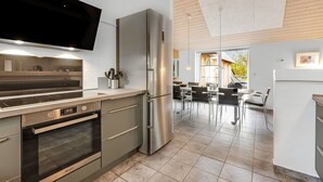 A modern kitchen with stainless steel appliances, a flat-screen TV, and a dining area with a view of the outdoors. - "Benthe" -  from the sea by Interhome (Ulfborg)