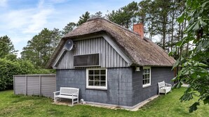 Une maison rustique avec un toit de chaume, une antenne parabolique et un banc dans la cour.