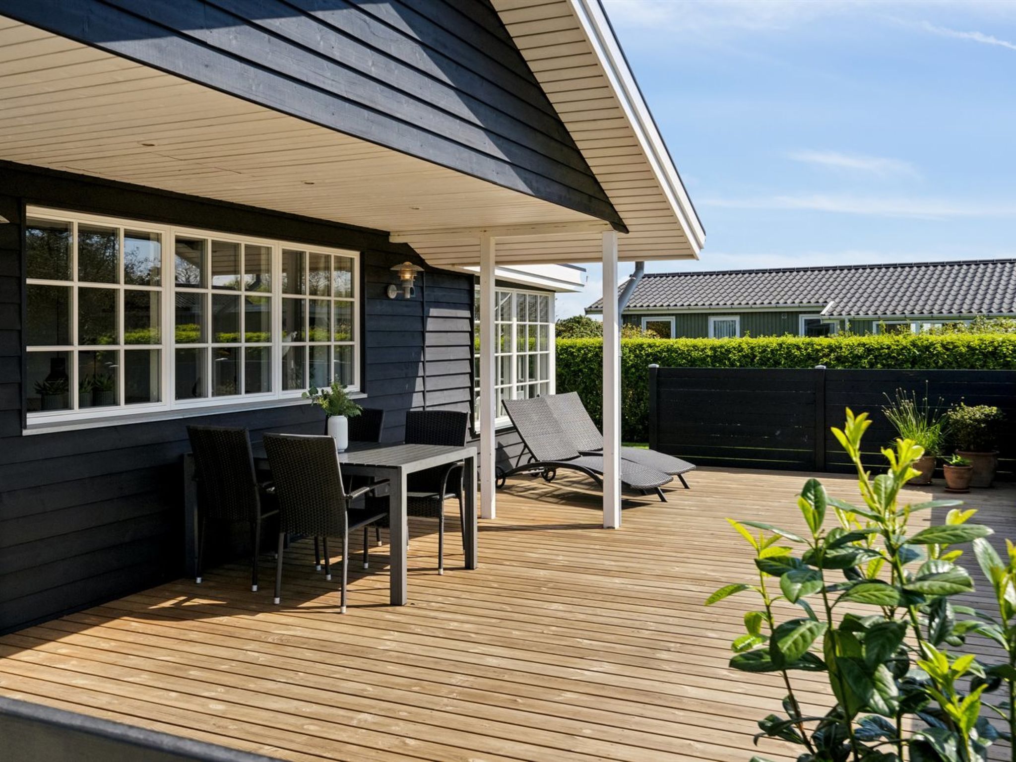 A covered patio with a table and chairs, a small garden area with potted plants, and a view of a neighboring house.