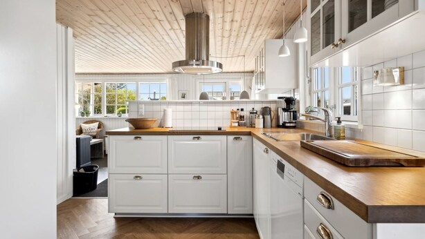 A modern kitchen with white cabinetry, a wooden herringbone floor, and a large island with a built-in sink. - "Ekatarina" - 125m from the sea by Interhome (Juelsminde)
