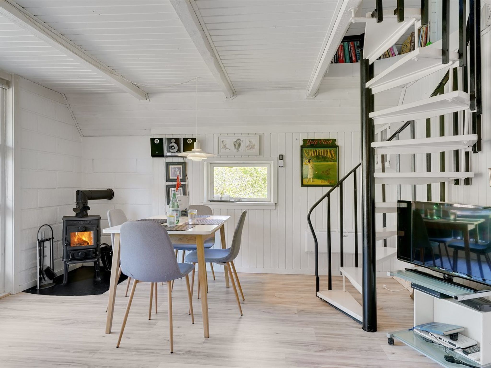 A cozy living room with a fireplace, a dining area with chairs, a bookshelf, and a TV.