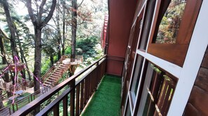 A balcony with a wooden railing, a small seating area, and a view of a forested area. - Pijar Resort Powered by Cocotel (Colo)