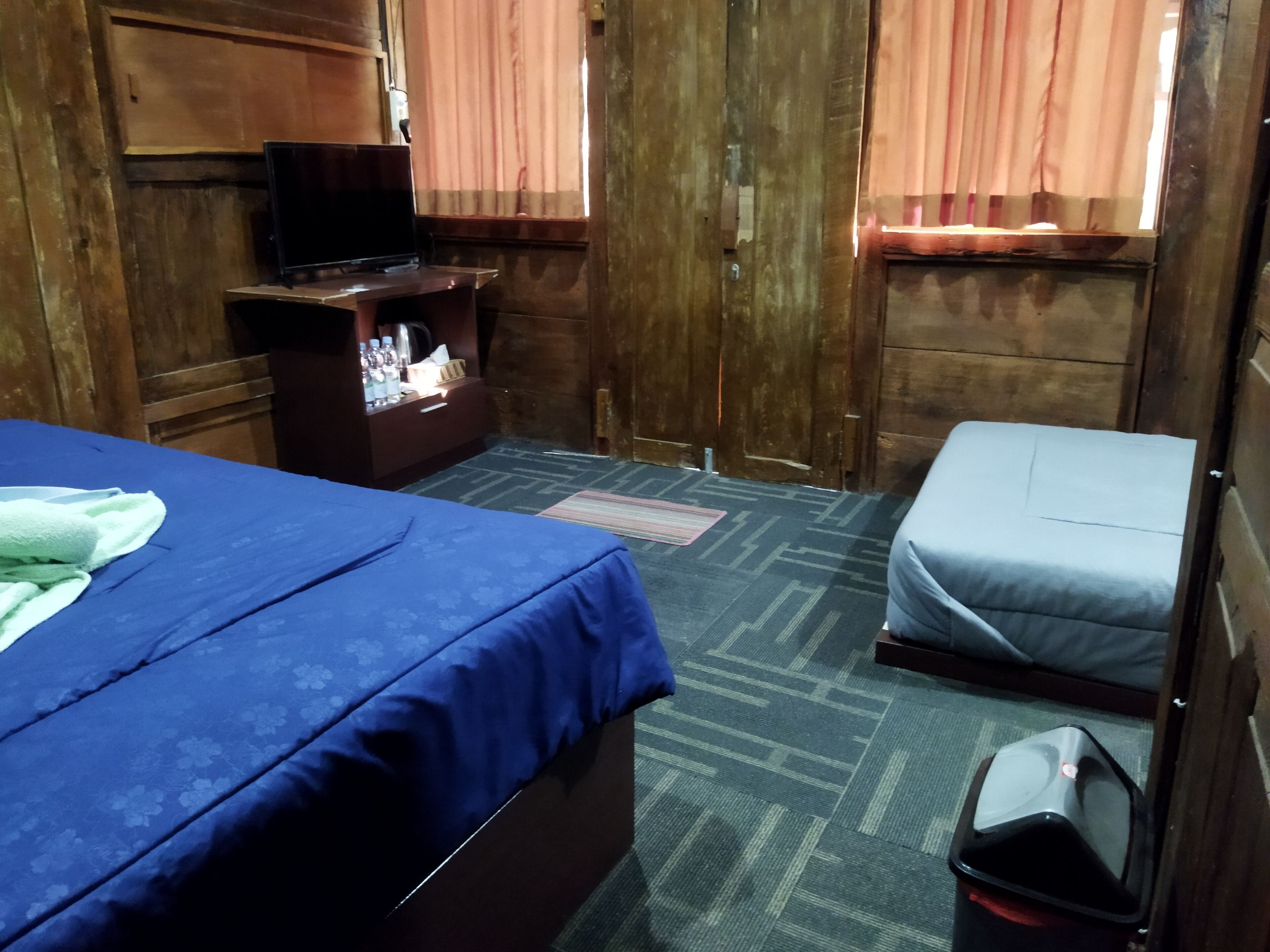 A room with a bed, a small table with toiletries, a bench, and a trash bin.