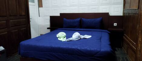 A hotel room with a large bed, a wooden headboard, and a white tiled wall.
