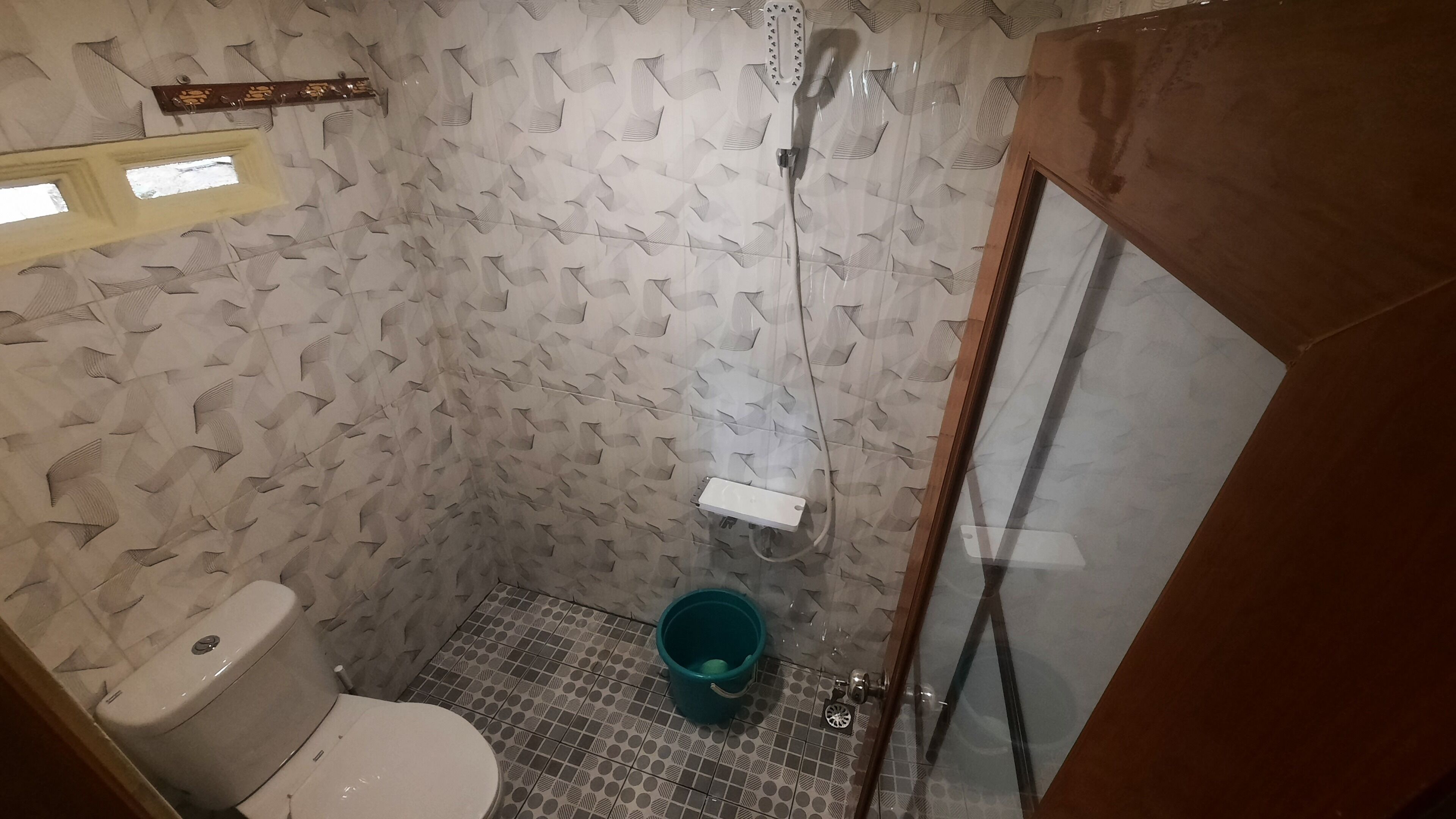 Une petite salle de bain avec des toilettes, une douche et un seau.