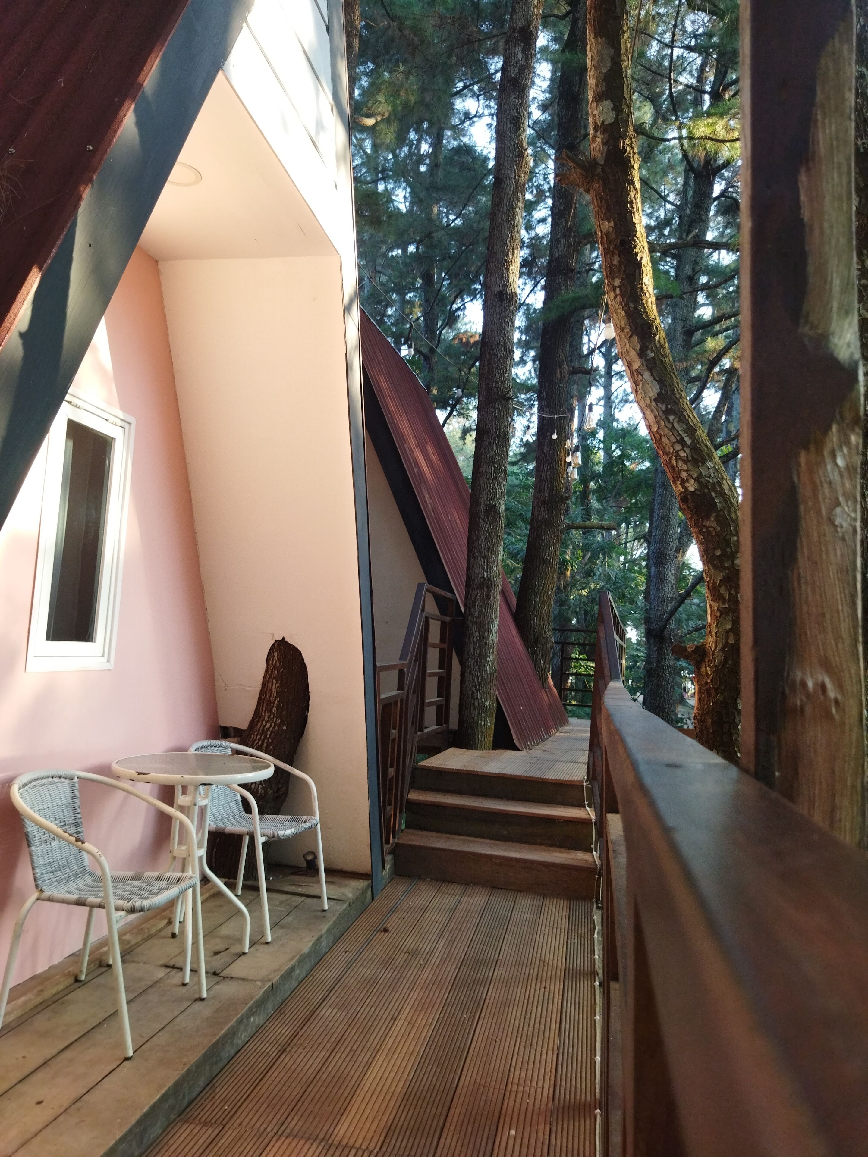A wooden deck with a table and chairs, a staircase leading to a covered area, and a view of the surrounding forest.