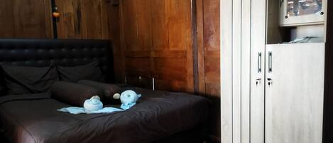 A bedroom with a large bed, wooden wardrobe, and a small window.